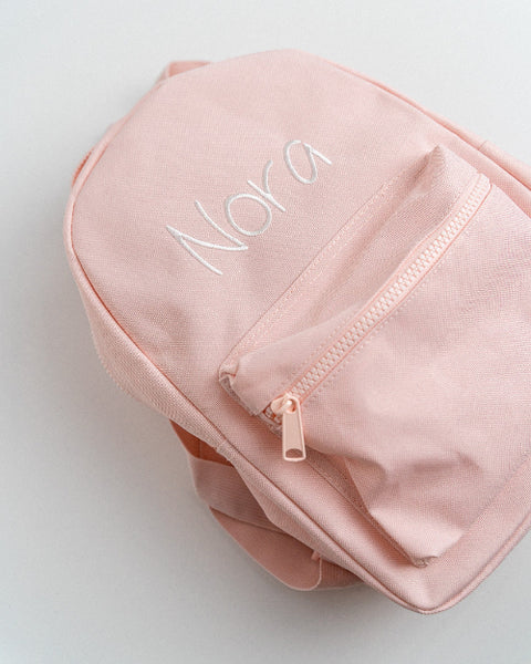 roze rugzakje met rits geborduurd met witte letters met de naam Nora